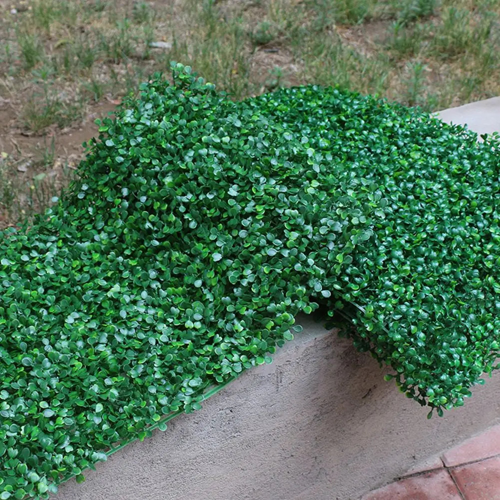 Dense green artificial grass hedge panels covering a retaining wall for privacy and decoration.