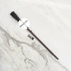 A dark metal magic wand replica with a textured handle and a circular metal core resting on a white marble surface.