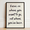 Black framed canvas print with white handwritten text that reads Focus on where you want to go not where you've been.
