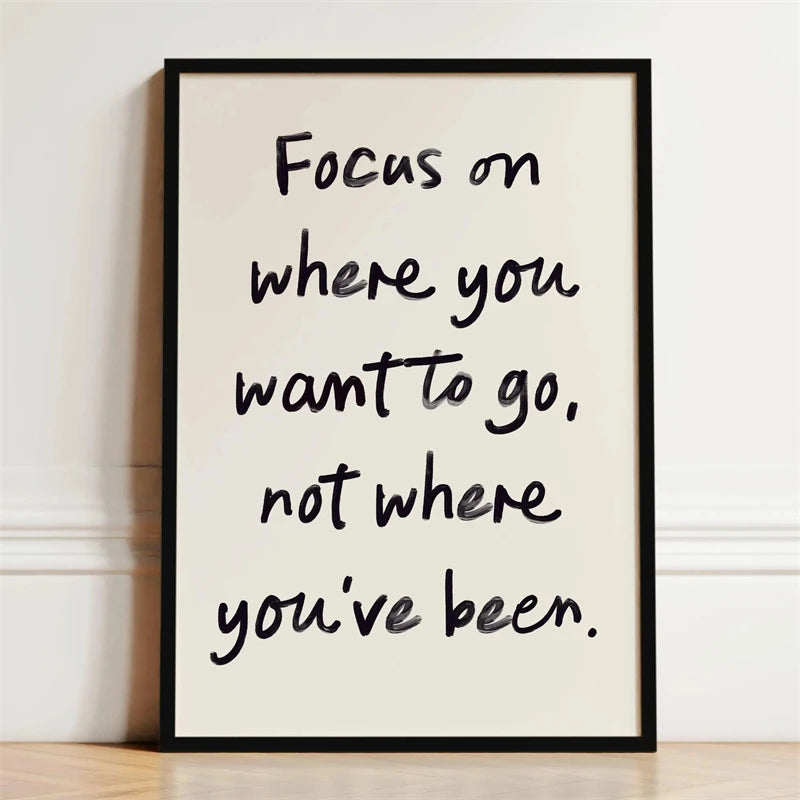 Black framed canvas print with white handwritten text that reads Focus on where you want to go not where you've been.
