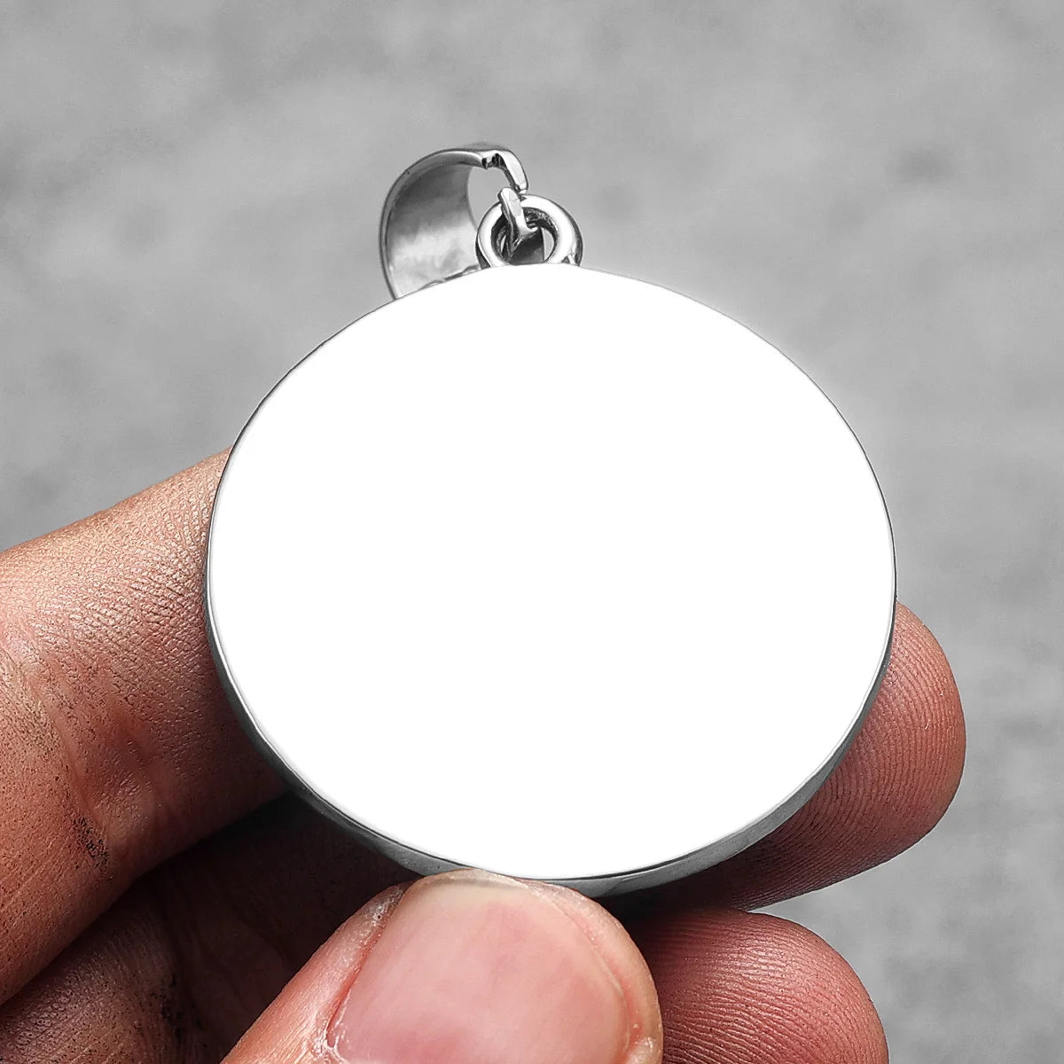 A silver stainless steel punk cross necklace pendant is held in a hand against a gray background.