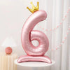 A pink foil number balloon shaped like the number six with a gold crown on top
