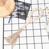 A beige wooden bead necklace with a natural fiber tassel displayed on a black grid background.