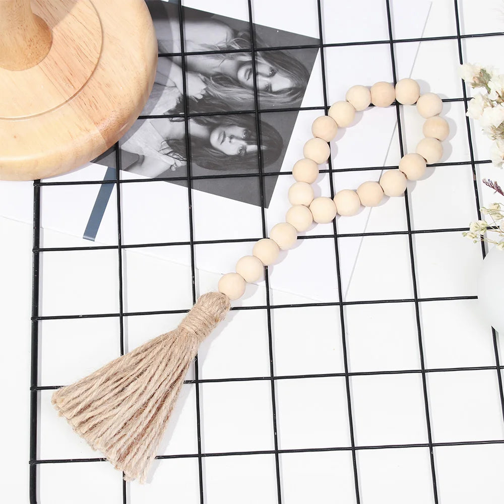 A beige wooden bead necklace with a natural fiber tassel displayed on a black grid background.