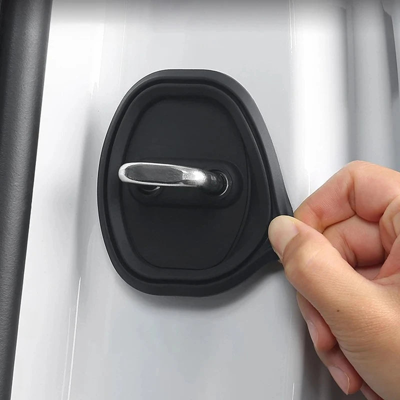 A hand is operating a black silicone door lock protector on a white car door panel.