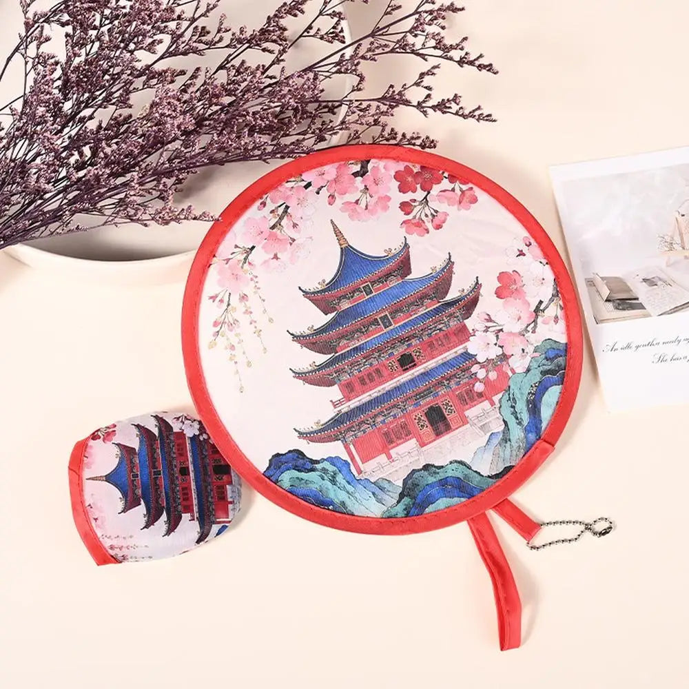 A pink and red fabric fan with a decorative design is shown next to some dried flowers.
