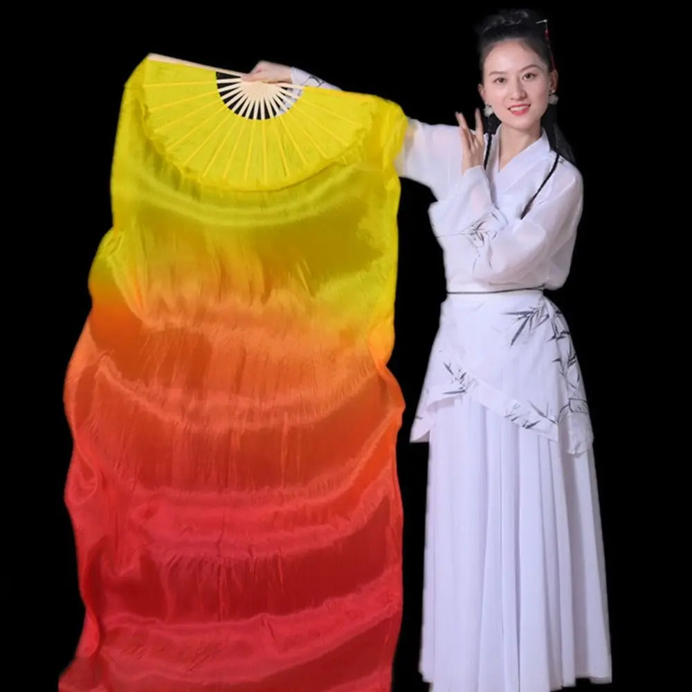 A woman in a white outfit holds a large silk ribbon dance fan with a gradient yellow to orange color.