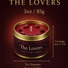 A tin candle labeled The Lovers in a gold tin with red wax and dried fruit, set against a dark background.
