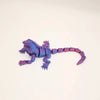 A purple articulated 3D printed lizard figurine lying on a white surface.