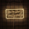 A glowing neon sign shaped like You're like really pretty hangs against a dark grid background.
