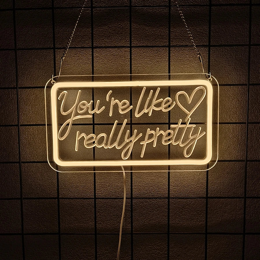 A glowing neon sign shaped like You're like really pretty hangs against a dark grid background.