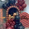 A close-up of a balloon arch display featuring burgundy and black latex balloons for a birthday celebration.