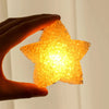 A hand holds an orange LED star light illuminating a dark background.
