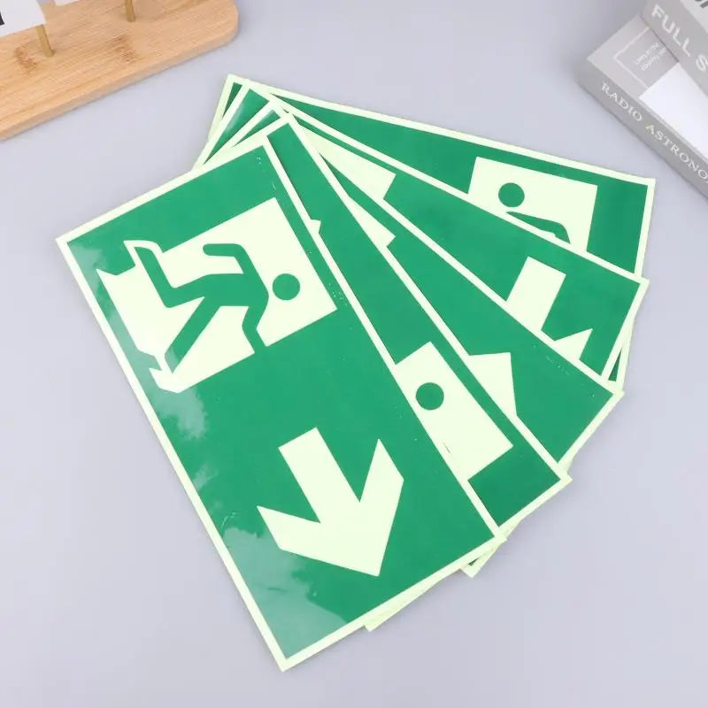 A stack of photoluminescent emergency exit sign decals in green and white on a light gray surface.
