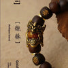 A close-up of a handcrafted Pixiu bracelet featuring dark wood beads and an antique brass charm.