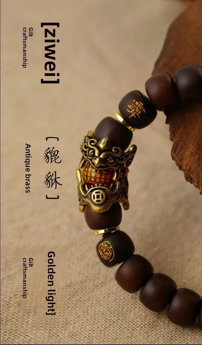 A close-up of a handcrafted Pixiu bracelet featuring dark wood beads and an antique brass charm.