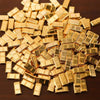 A pile of small, rectangular simulated gold bars scattered on a dark surface.