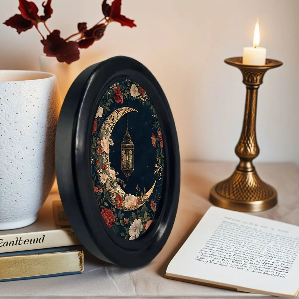 A dark oval frame featuring a detailed gothic Victorian flower and moon design sits on a table next to a lit candle.