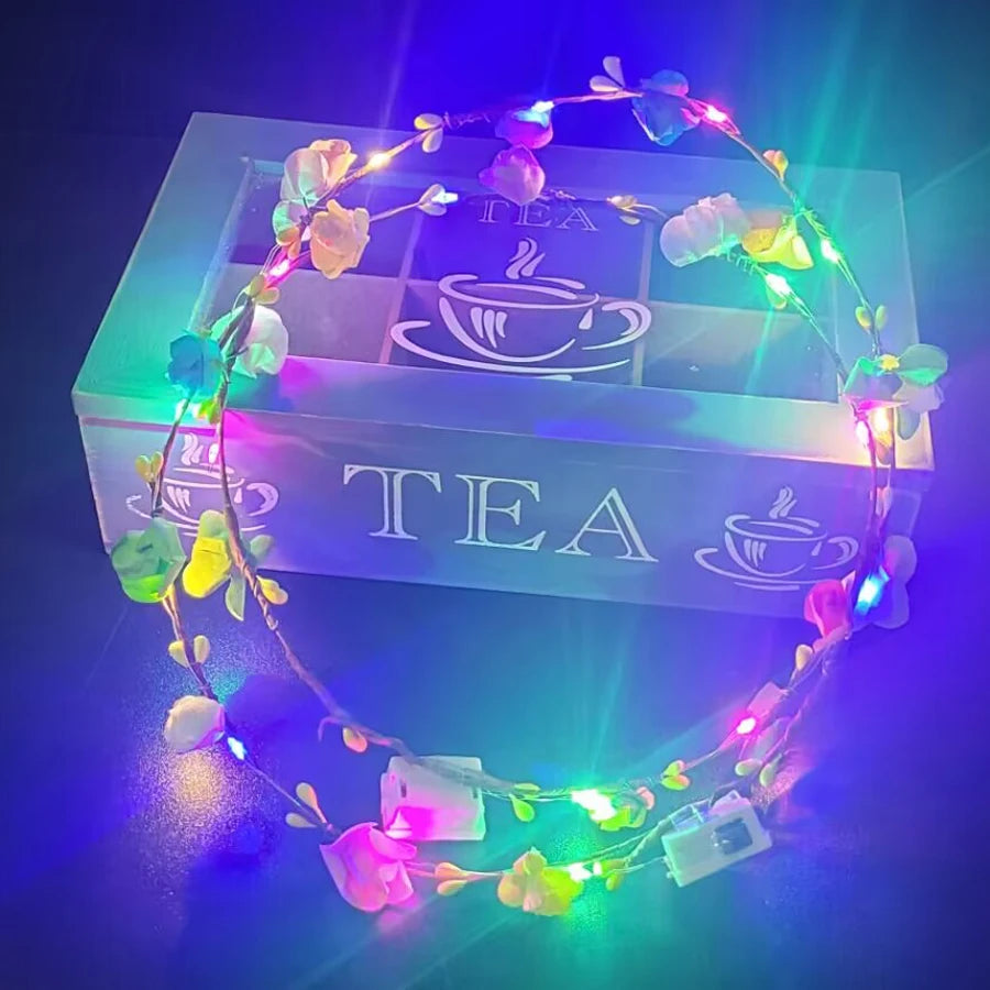 A glowing flower wreath headband with ten LEDs rests inside a square box illuminated with purple and green light.