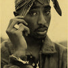 A close-up portrait of a man wearing a patterned headwrap and a jacket, holding his face with his hand.