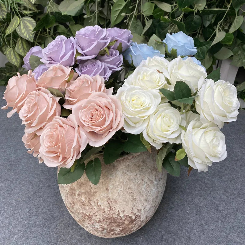A bouquet of silk roses in shades of lavender, blue, and cream arranged in a textured stone pot.
