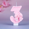 Glittery pink number three birthday candle with a decorative bow on a white base