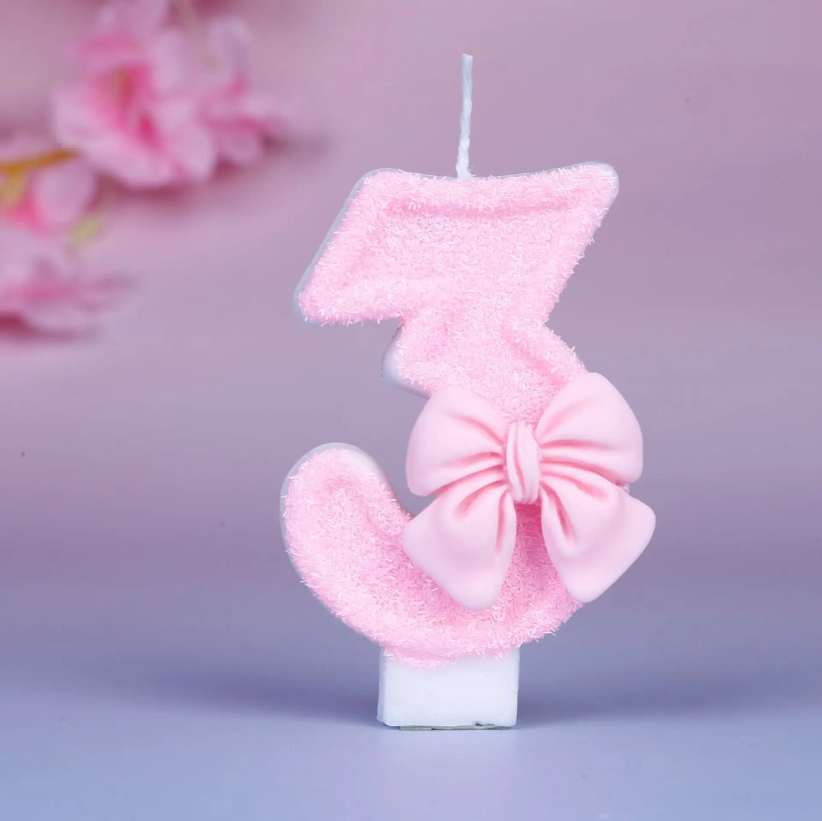 Glittery pink number three birthday candle with a decorative bow on a white base