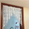 A sheer white beaded lace valance curtain hanging in a wooden frame over a mirror.