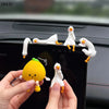 A hand holds a yellow resin cartoon duck figurine next to several white ceramic duck figurines on a black surface.