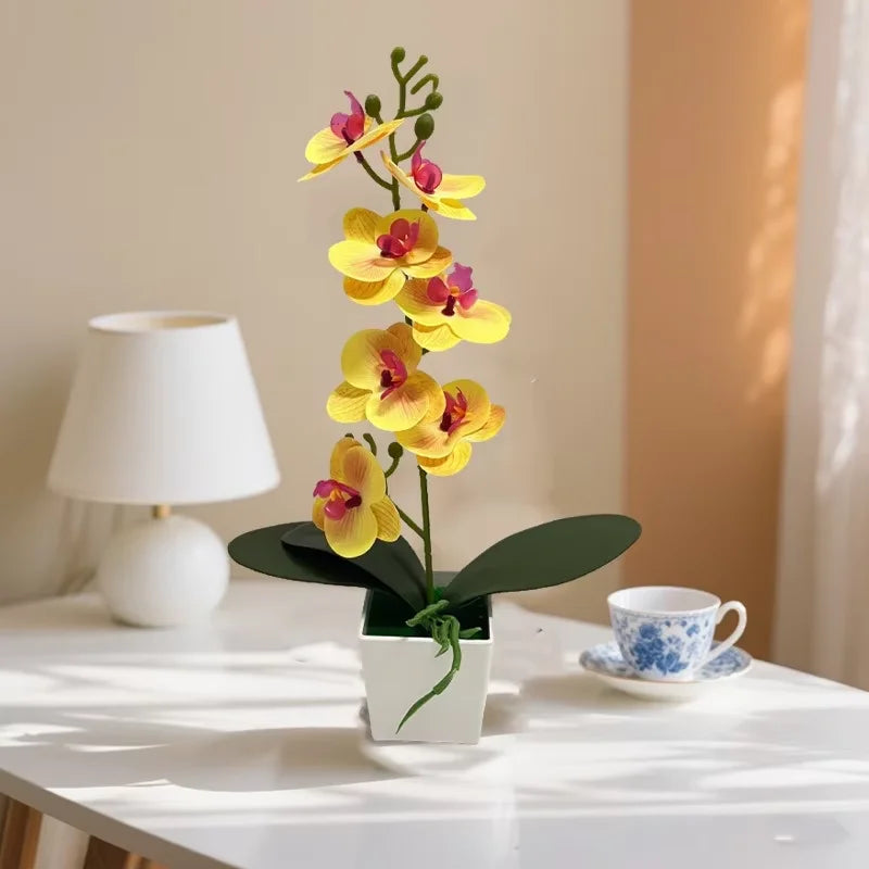 A small potted artificial plant with yellow and pink flowers displayed on a white table.