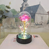 Une rose de verre éternelle avec une lumière LED est exposée sur une surface blanche devant un arrière-plan d'église et de pa