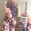 A balloon garland arch featuring shades of pink and purple balloons with a purple floral accent.