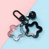 A colorful star charm pendant keychain with a clear glass element and black metal components on a light pink and blue backgro