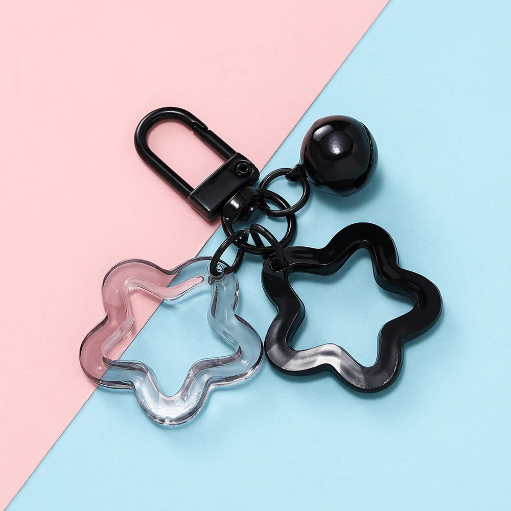 A colorful star charm pendant keychain with a clear glass element and black metal components on a light pink and blue backgro