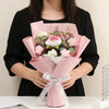 A pink handmade crochet rose flower bouquet is held by a person against a white background.