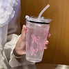 A hand holds a clear pink plastic cup with a lid and straw, decorated with pink bow patterns.
