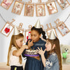 Three young girls interacting with a banner displaying monthly growth records for a baby's first birthday.