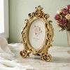Vintage gold oval resin picture frame with a floral design displayed on a marble surface.