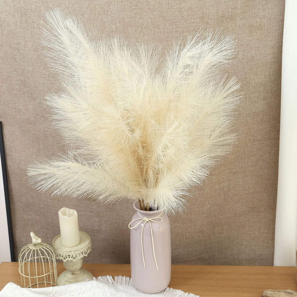 A dried artificial pampas grass bouquet in a pink vase displayed on a wooden surface.