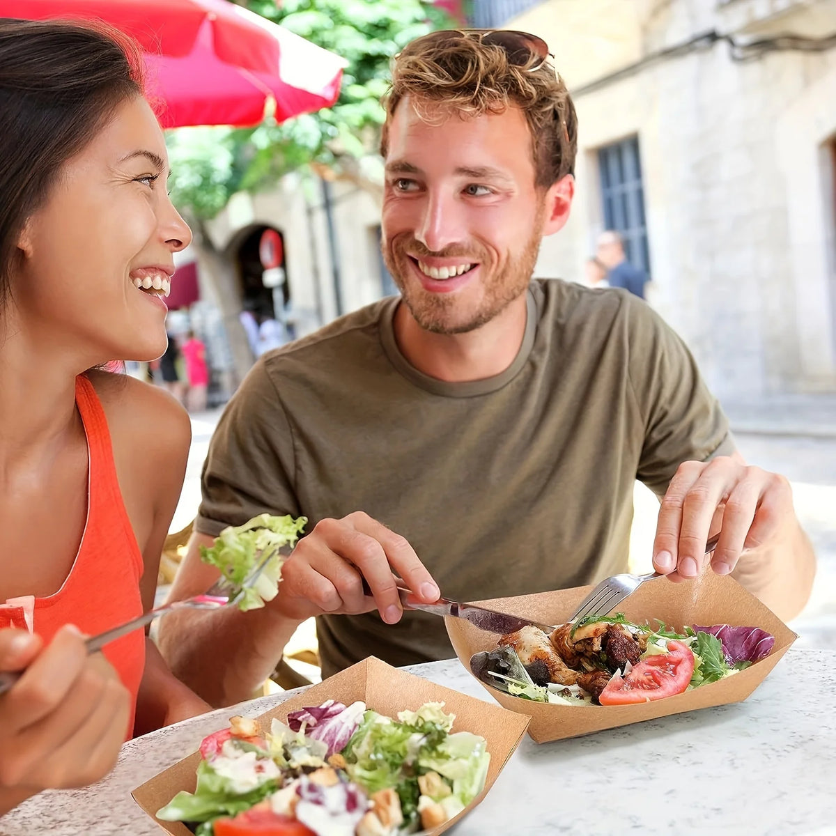 A man and a woman smiling while sharing food served in kraft paper disposable serving boats.