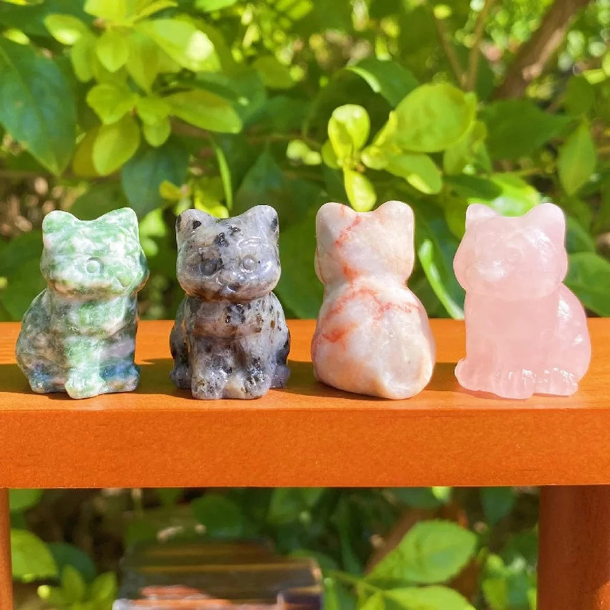 Quatre ornements de chats en cristal sculptés à la main dans des tons de vert, gris, rose et blanc, posés sur une surface ora