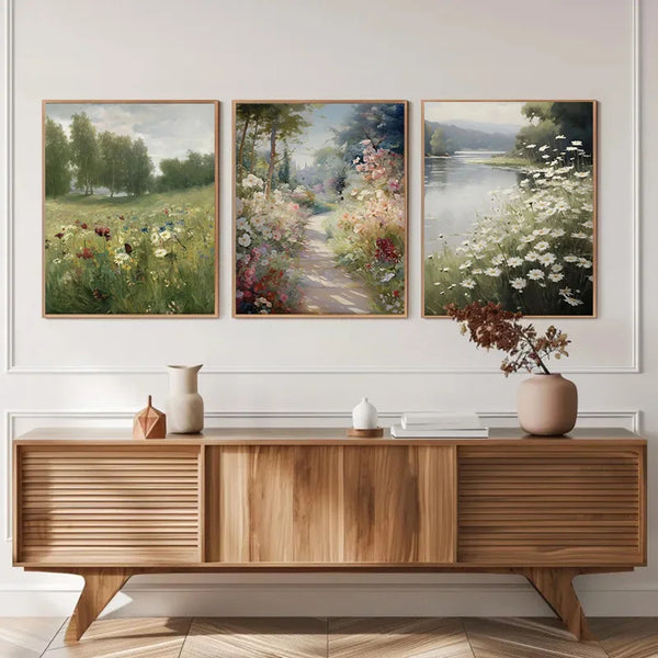 A gallery wall featuring three paintings of countryside spring flowers above a wooden cabinet.