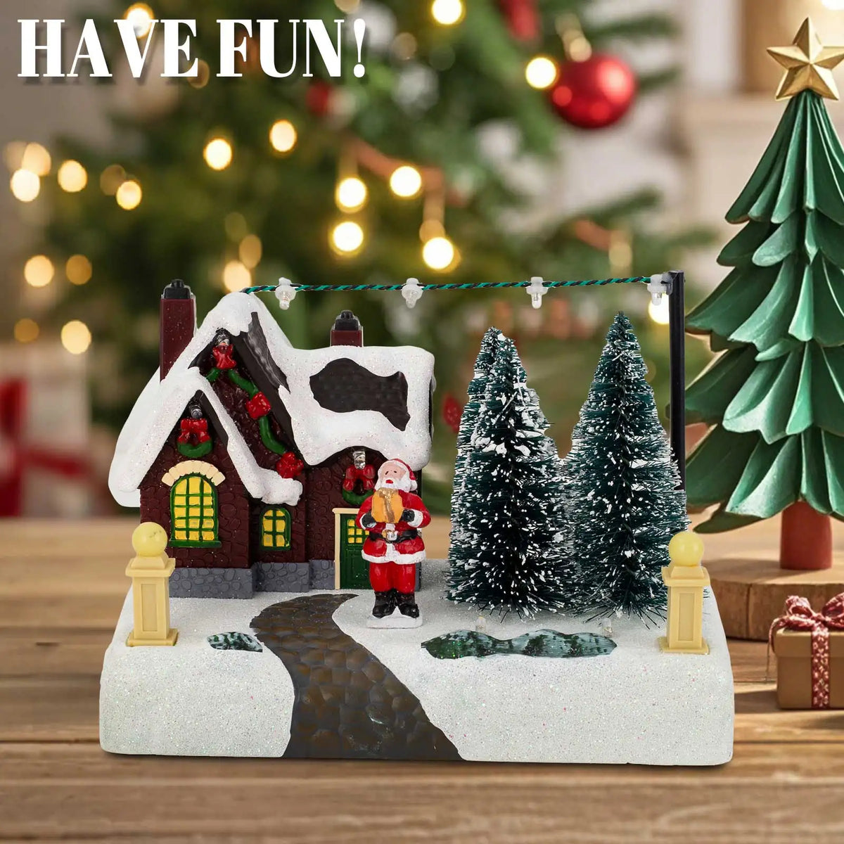 Illuminated Christmas village scene featuring a snowy house, Santa, and evergreen trees.