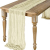A semi-sheer gauze table runner in sage green draped over a wooden table.