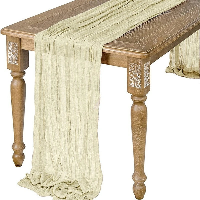 A semi-sheer gauze table runner in sage green draped over a wooden table.