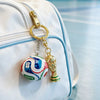 A gold-colored FIFA trophy keychain is attached to a white backpack.
