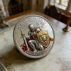 A silver coin featuring a 3D carved lion warrior with a sword and shield, surrounded by text.