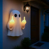 A white ghost figurine lamp with a warm glow is mounted on a wall next to a dark door.