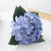 A bouquet of artificial light blue hydrangea flowers with green leaves.