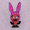 A pink enamel pin badge featuring a cartoon character with large eyes and a wide smile.
